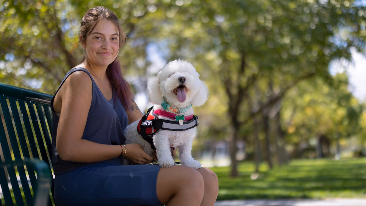 Woman on a park bench with her small white service dog in a vest, PSD letter in Georgia